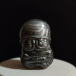 Figura Gogo Crazy Bones gris con acabado metálico, expresión seria y forma ovalada, sobre fondo oscuro