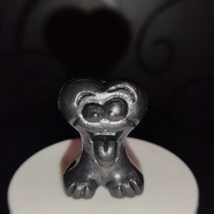 Figura Gogo Crazy Bones negra con acabado metálico, forma de corazón y expresión con lengua fuera, sobre fondo oscuro