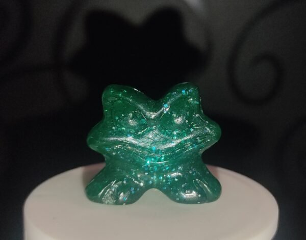 Figura Gogo Crazy Bones verde translúcido con purpurina sobre fondo oscuro, colocada sobre base blanca