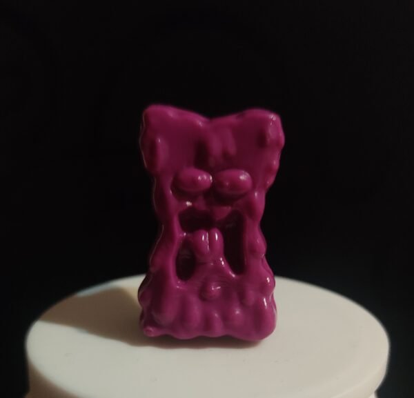 Figura original Gogo Crazy Bones color fucsia con diseño de expresión gruñona sobre fondo negro